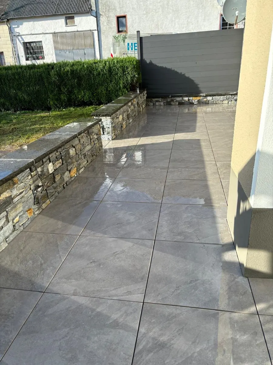 Moderne Terrasse mit glänzenden Feinsteinzeugfliesen und Natursteinmauer